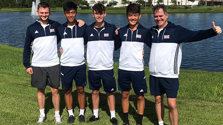 5 members of the GB team standing on grass in front of a pond with blue and white GB jackets on