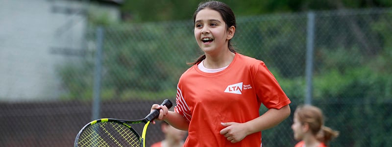 junior player on courting holding racket wearing a red LTA tennis top