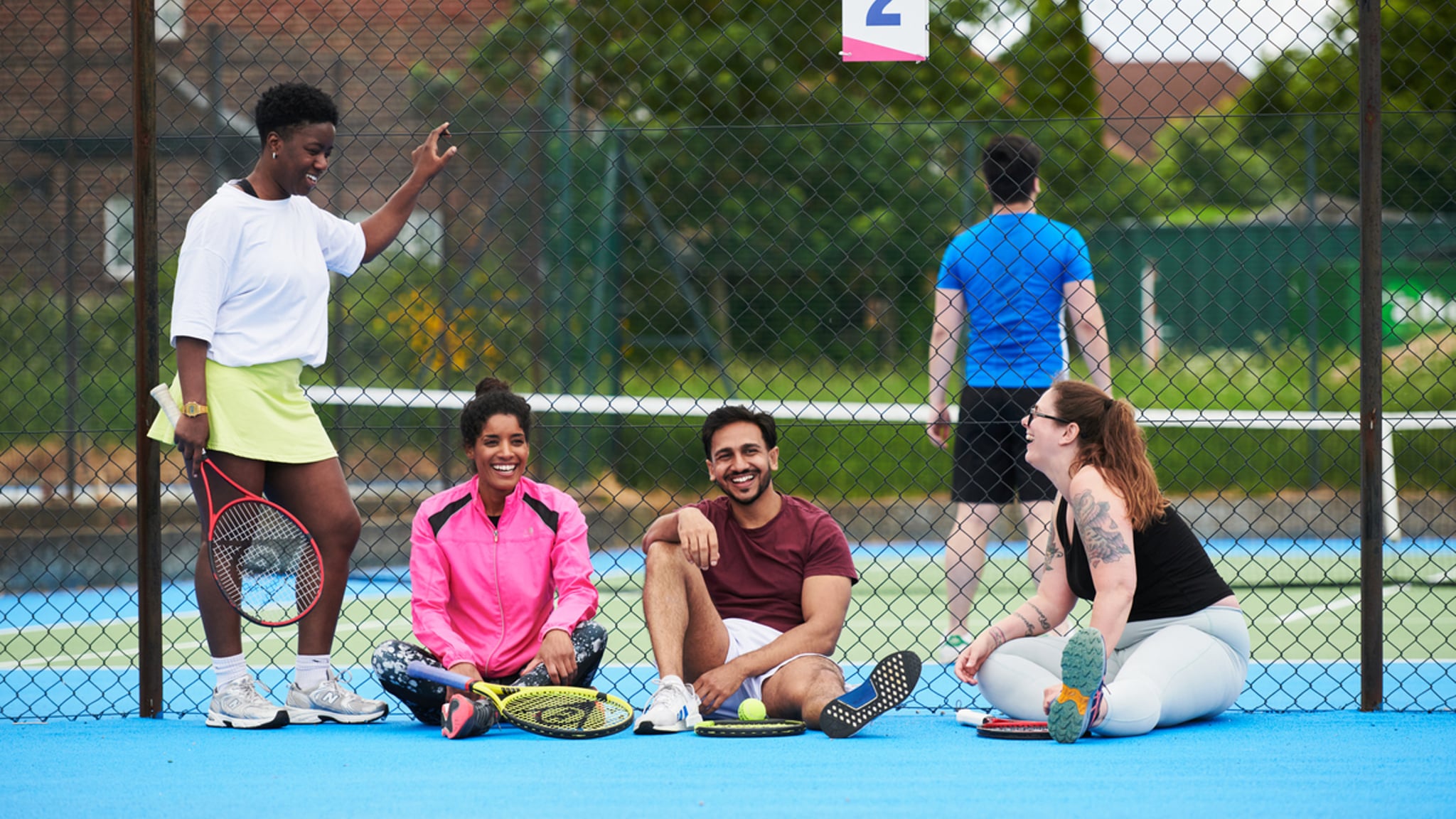 A group of people laughing together at the side of a public tennis court
