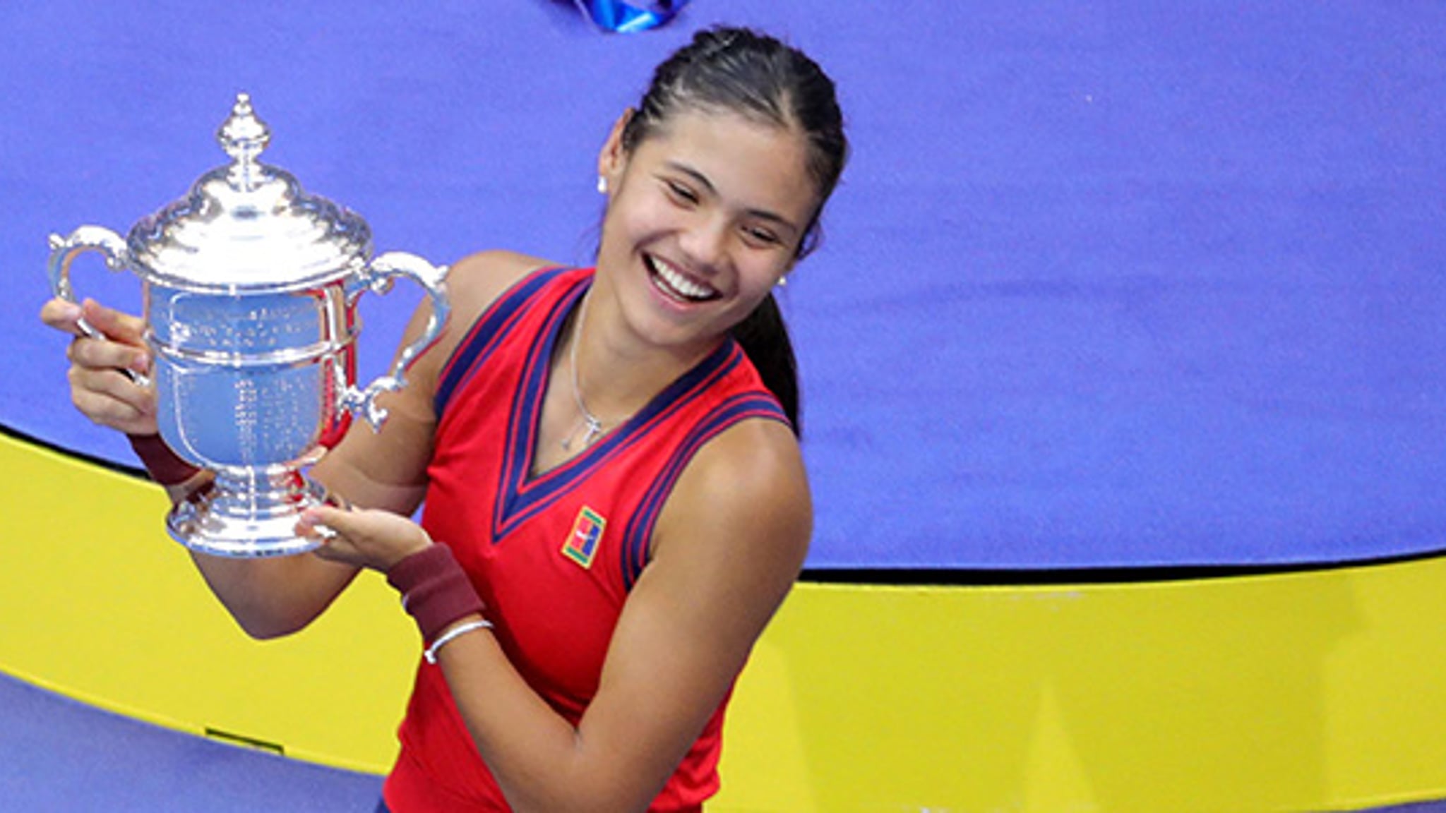 Emma Raducanu smiling and holding the 2021 US Open trophy