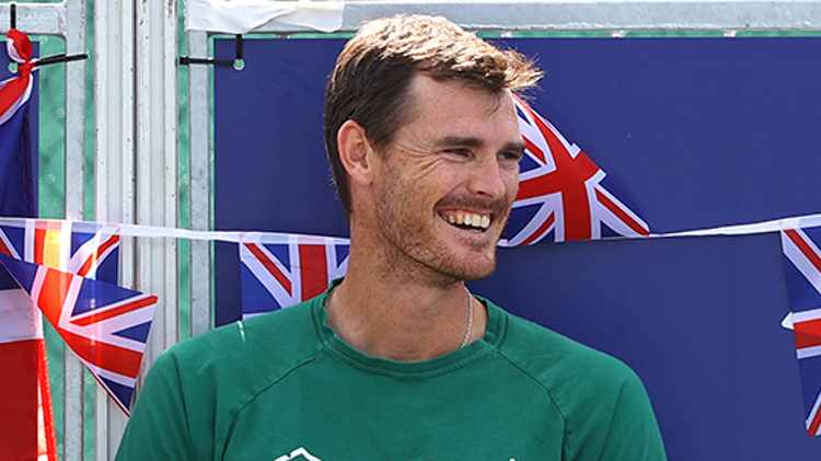 jamie murray smiling looking to the side with mini GB flags hanging  and LTA logo behind him 