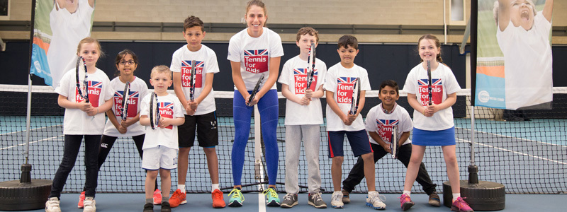 Johanna Konta with a group of children, all holding tennis rackets in front of a tennis net on a court
