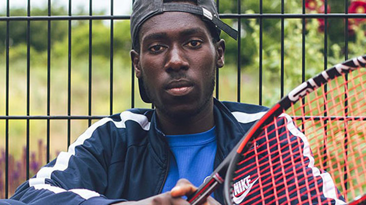 close up of Arum Akom sitting in front of a fence with tennis racket in hand