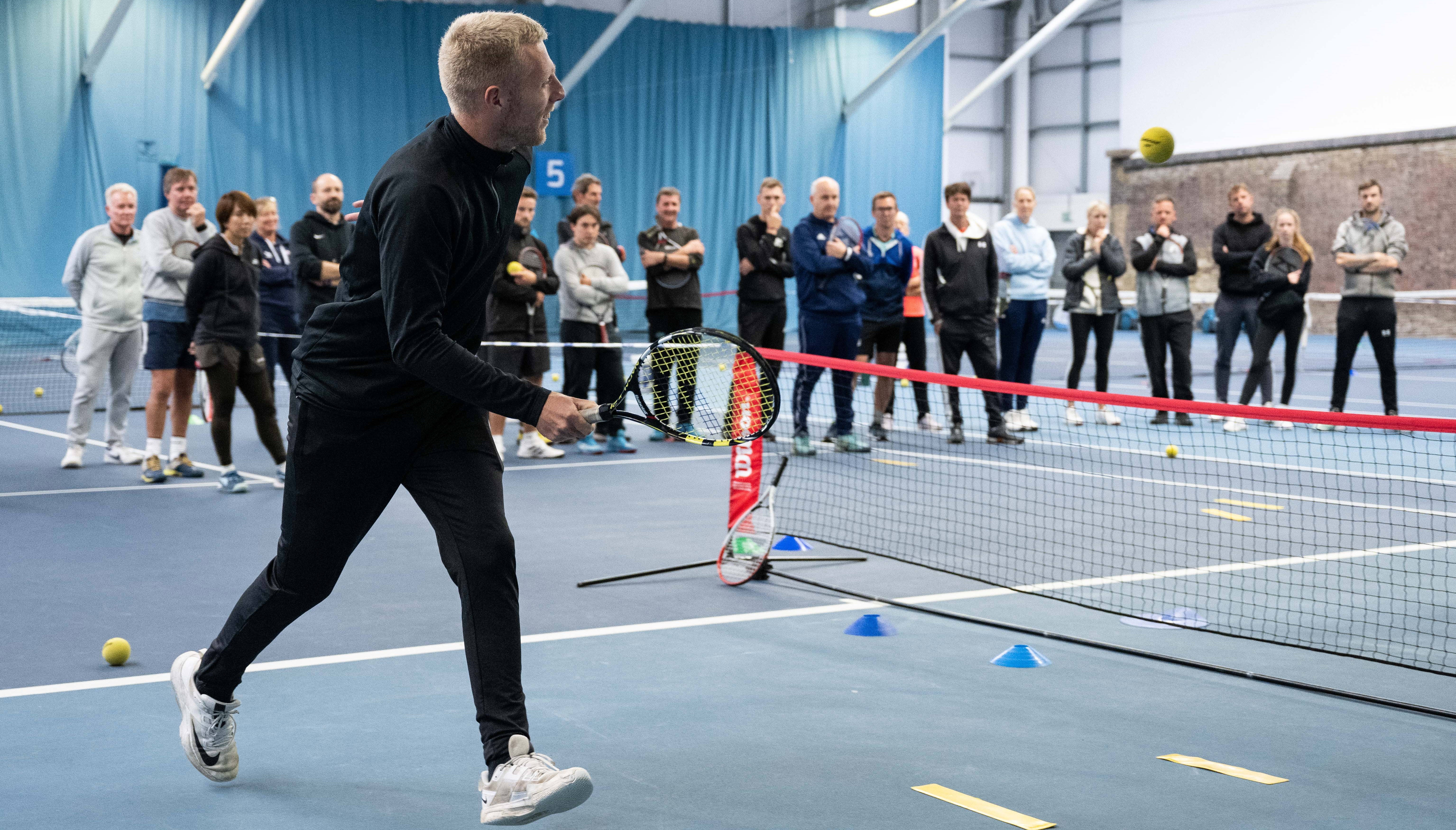 Male coach on mini tennis court demonstrating drill to crowd