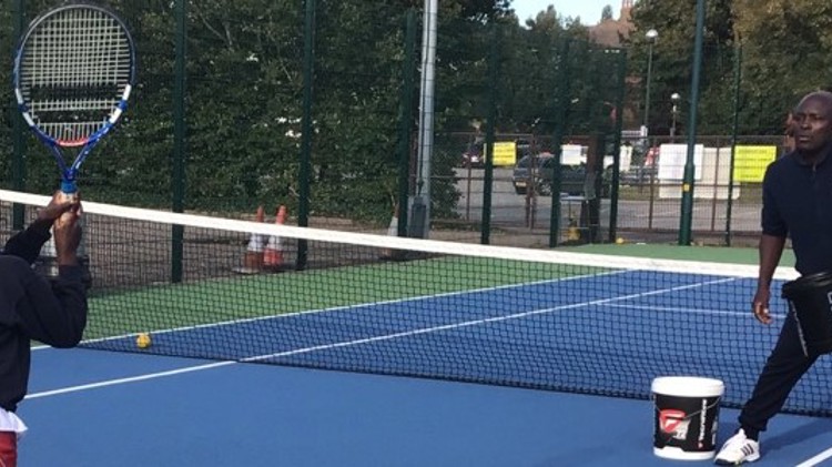 Isaac Frimpong coaching a young child tennis on an outdoor tennis court