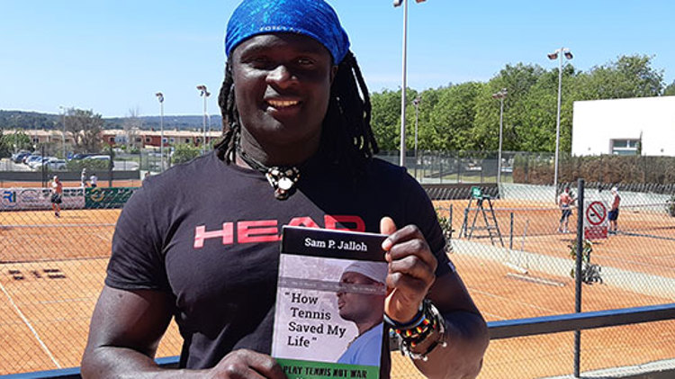 Sam Jalloh holding his book in front of tennis courts