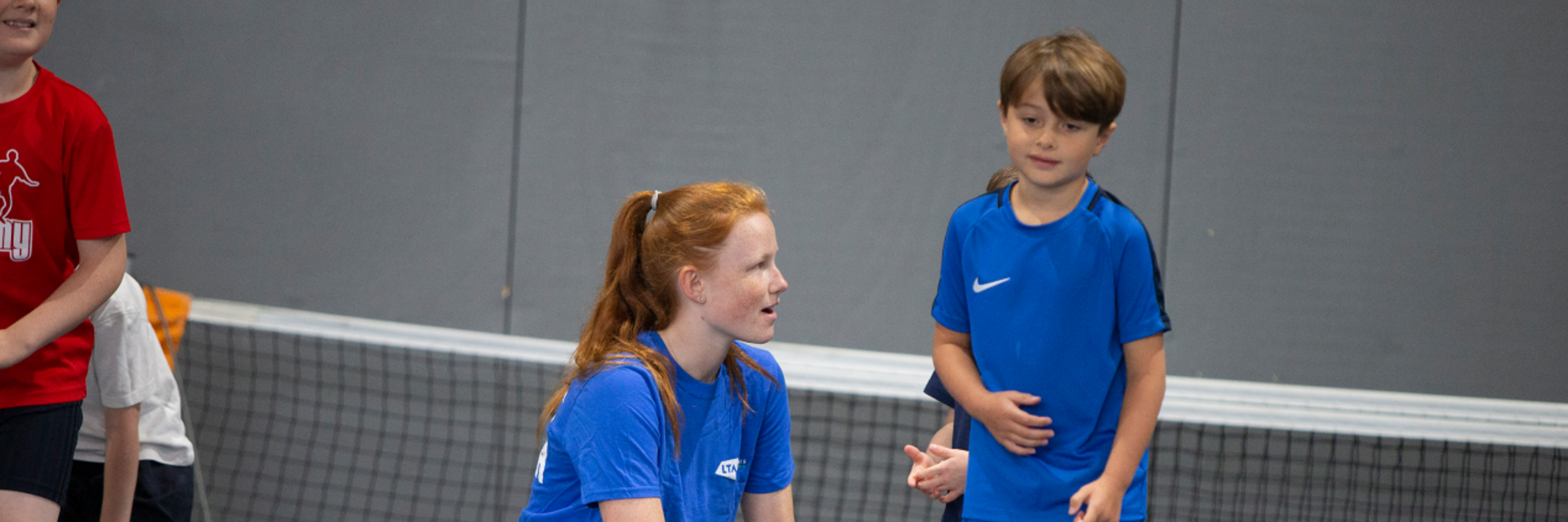 A Tennis Leader chats to a young boy while doing a game on a tennis court