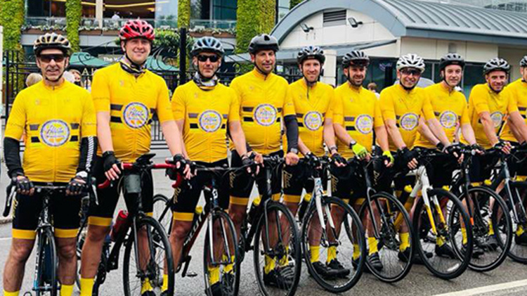 rutherglen peloton team standing on their bikes lined up outside wimbledon with yellow shirts and bike helmets on
